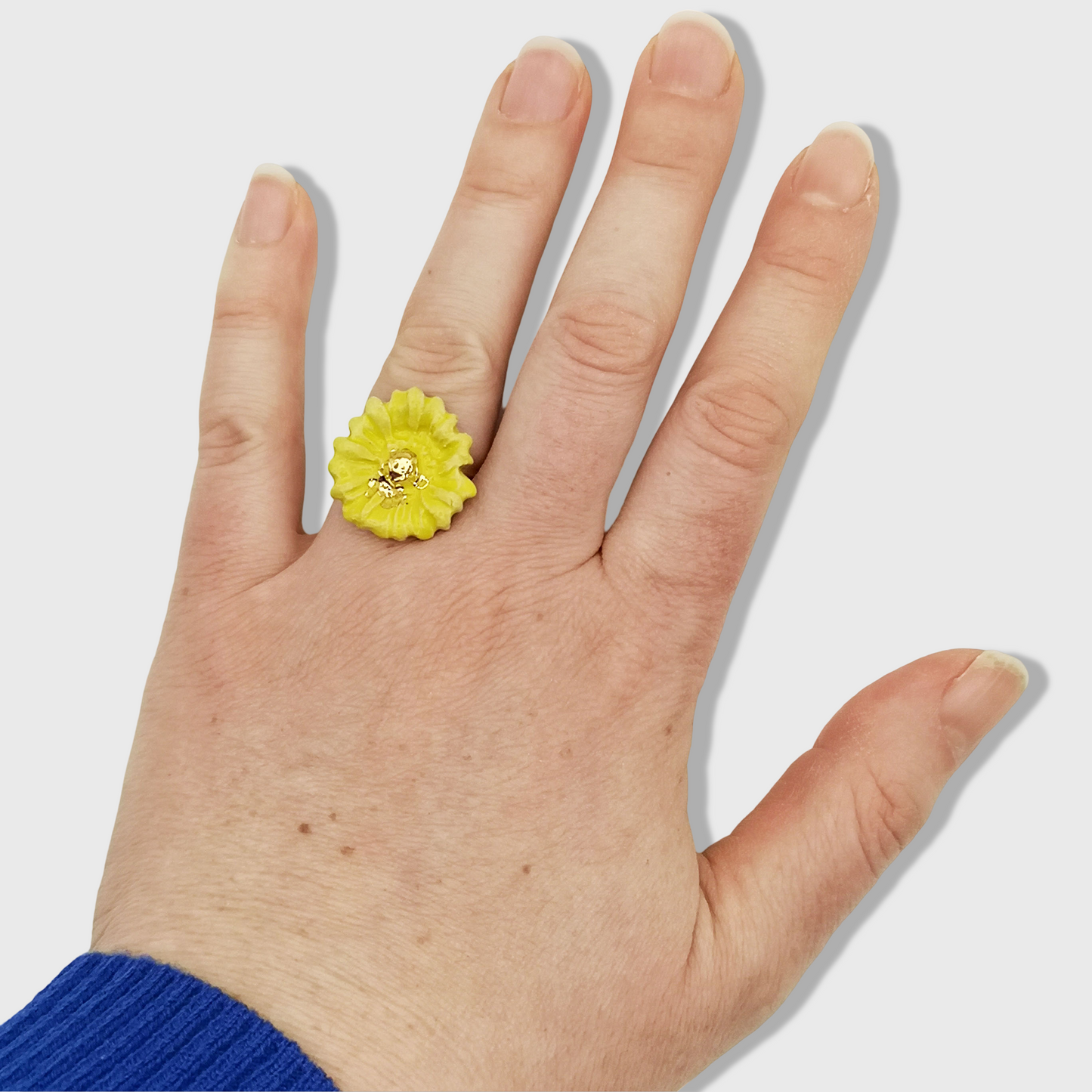 Bague artisanale avec une marguerite jaune et des touches dorées, présentée dans un écrin rose délicat."