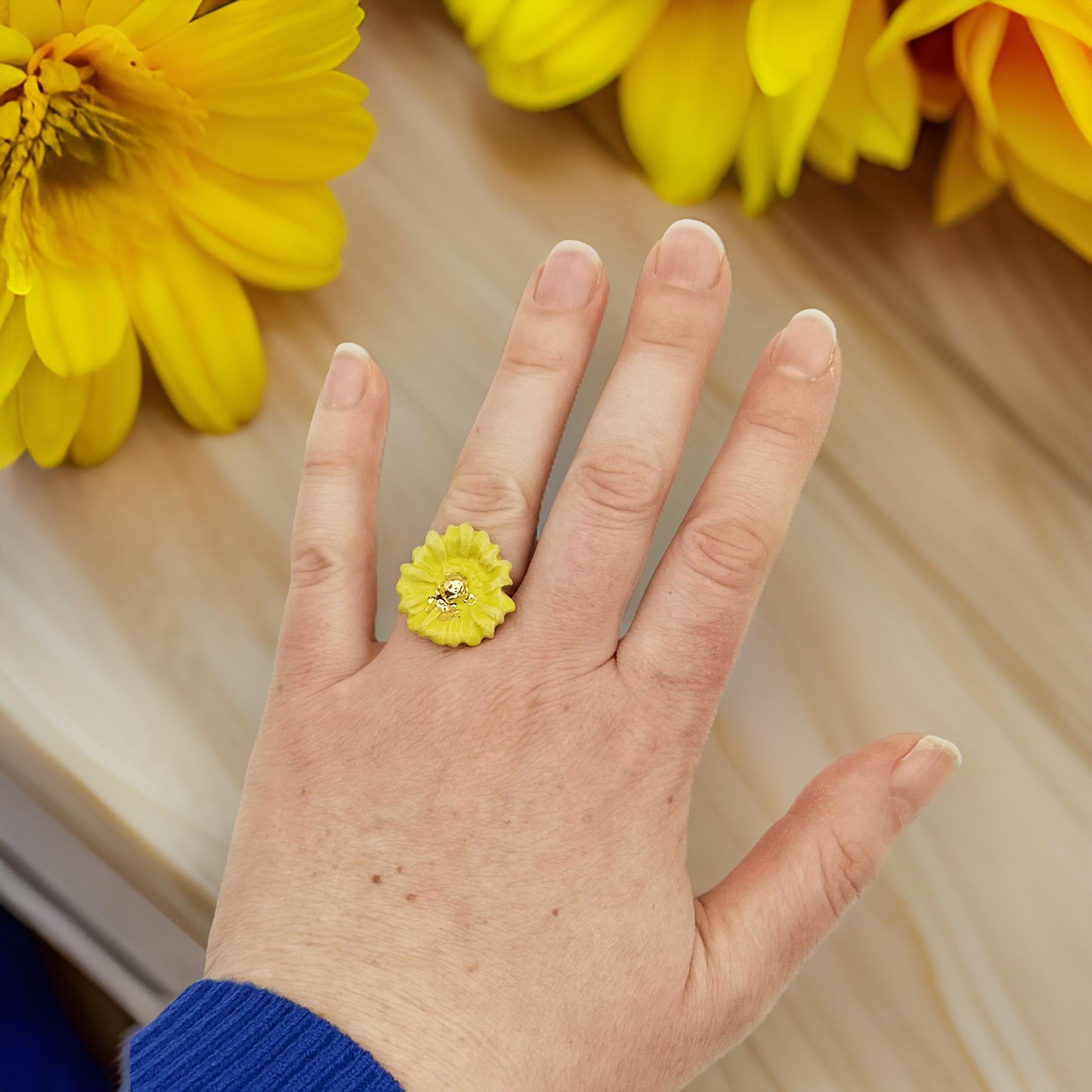 Bague unique en céramique avec un design de marguerite jaune, élégamment exposée sur un fond minimaliste.