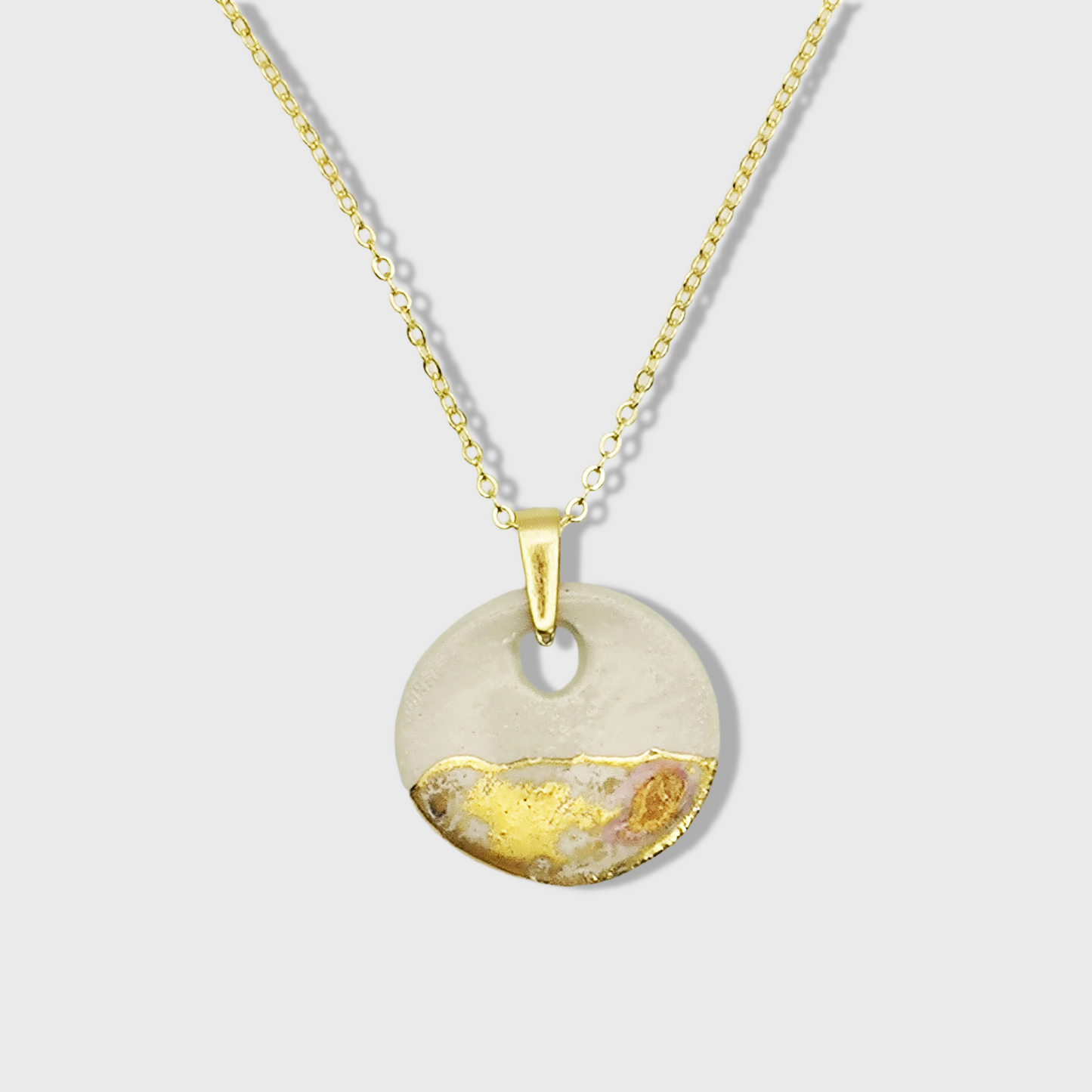 Collier médaillon blanc en argile et or sur une chaîne dorée, bijou artisanal élégant et raffiné.