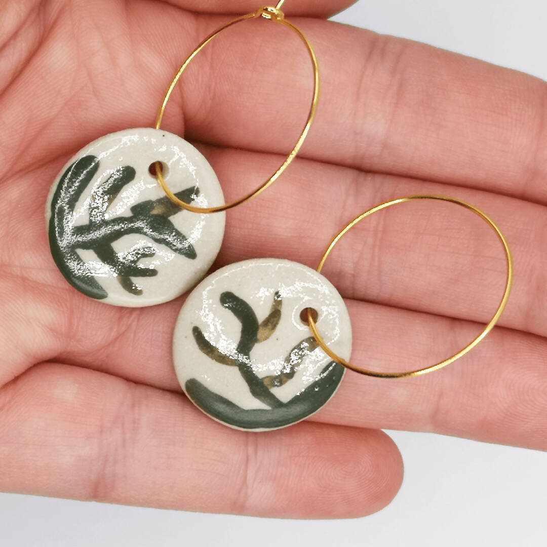 Bijoux en céramique faits main avec médaillon vert céladon et détails dorés, représentant des branches d'arbres et un style minimaliste.