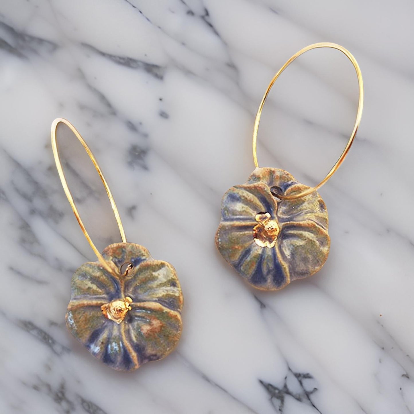 Photo des boucles d'oreilles pensée bleu et or, élégamment posées sur une table en marbre.