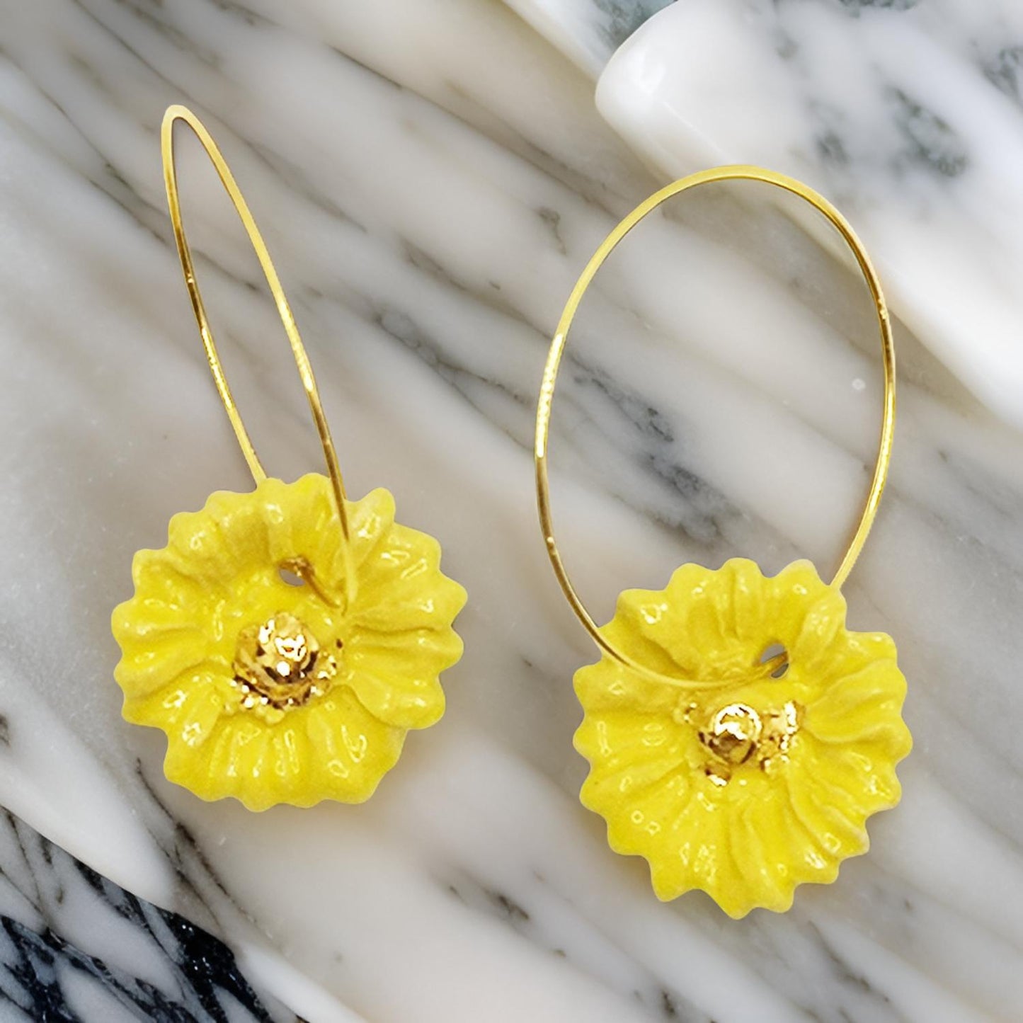 Photo de boucles d'oreilles fleur marguerite jaune vif et or, élégamment posées sur une table en marbre