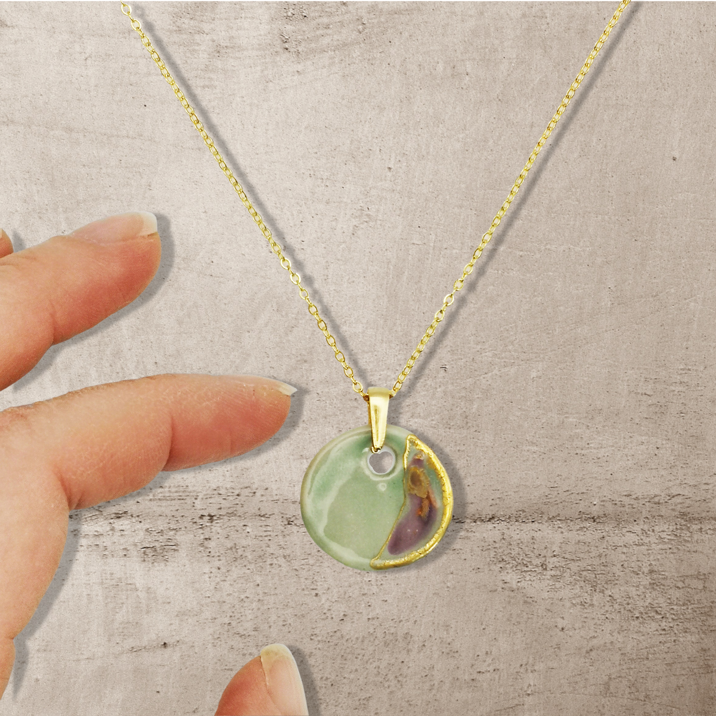 Gros plan sur le pendentif en céramique vert céladon avec des touches d'or, suspendu à une délicate chaîne dorée à l'or fin 24K. Un bijou artisanal au design unique.