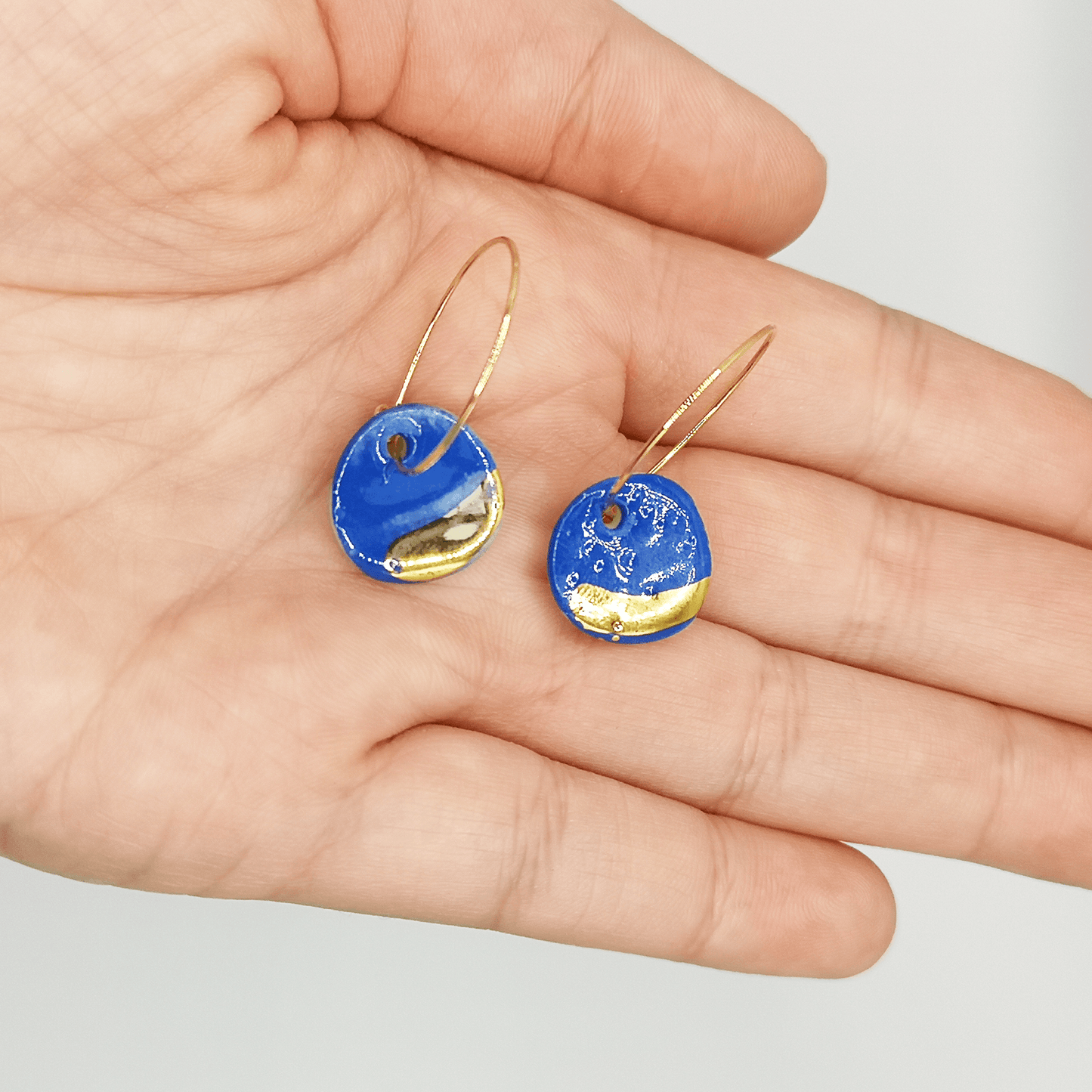 Boucles d'oreilles bleu Klein  or pendante pour femme dans une main