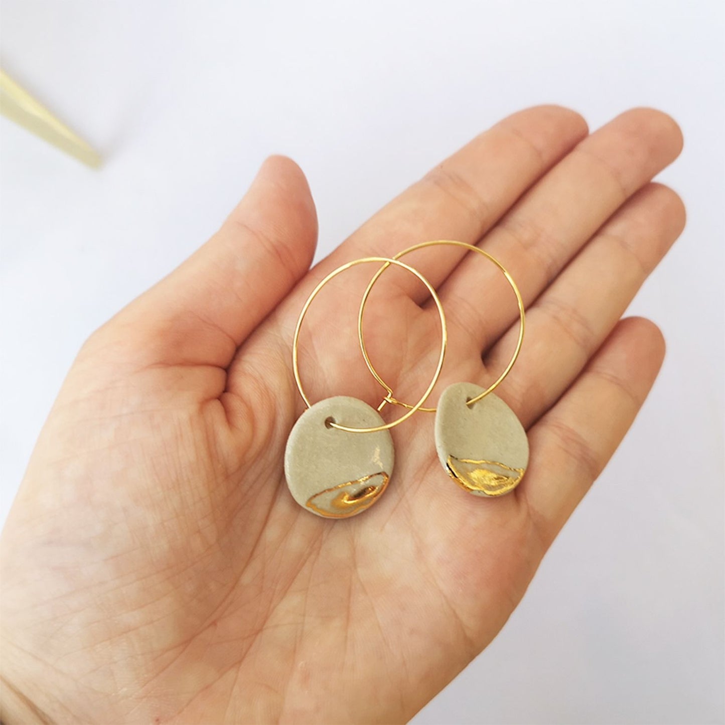 Détail des boucles d'oreilles en céramique émaillée blanche et or avec anneaux en laiton doré 24K