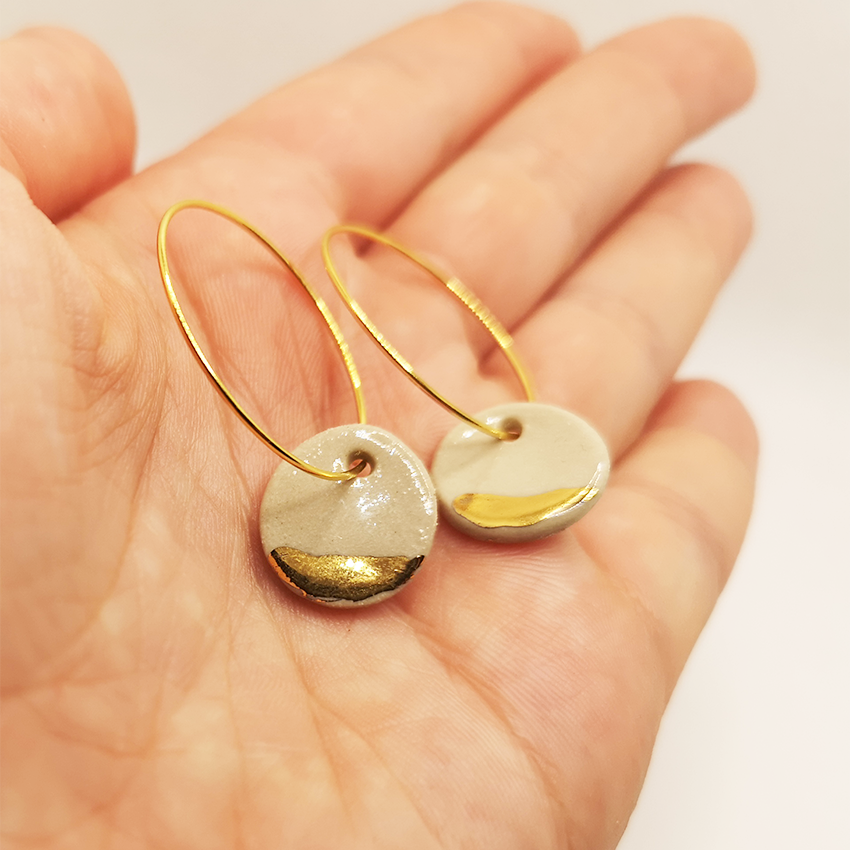 Boucles d'oreilles blanches argiles et or dans une main