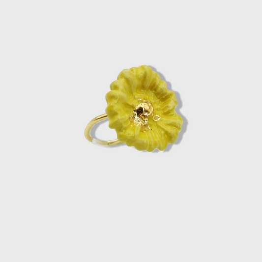 Bague artisanale avec une marguerite jaune et des touches dorées, présentée dans un écrin rose délicat.