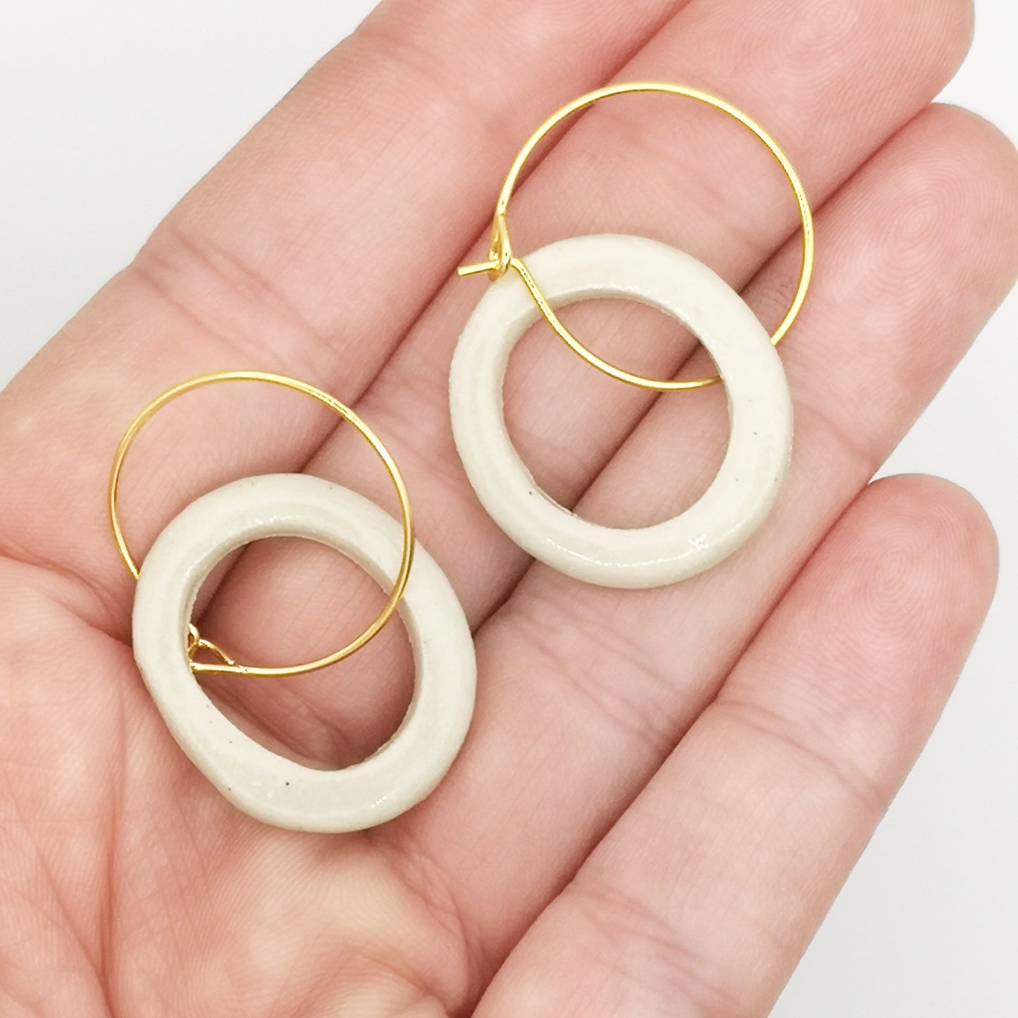 Vue rapprochée des boucles d'oreilles en céramique blanc argile - Gros plan des boucles d'oreilles minimalistes en céramique blanc argile avec montures en laiton doré, offrant élégance et simplicité à la fois.