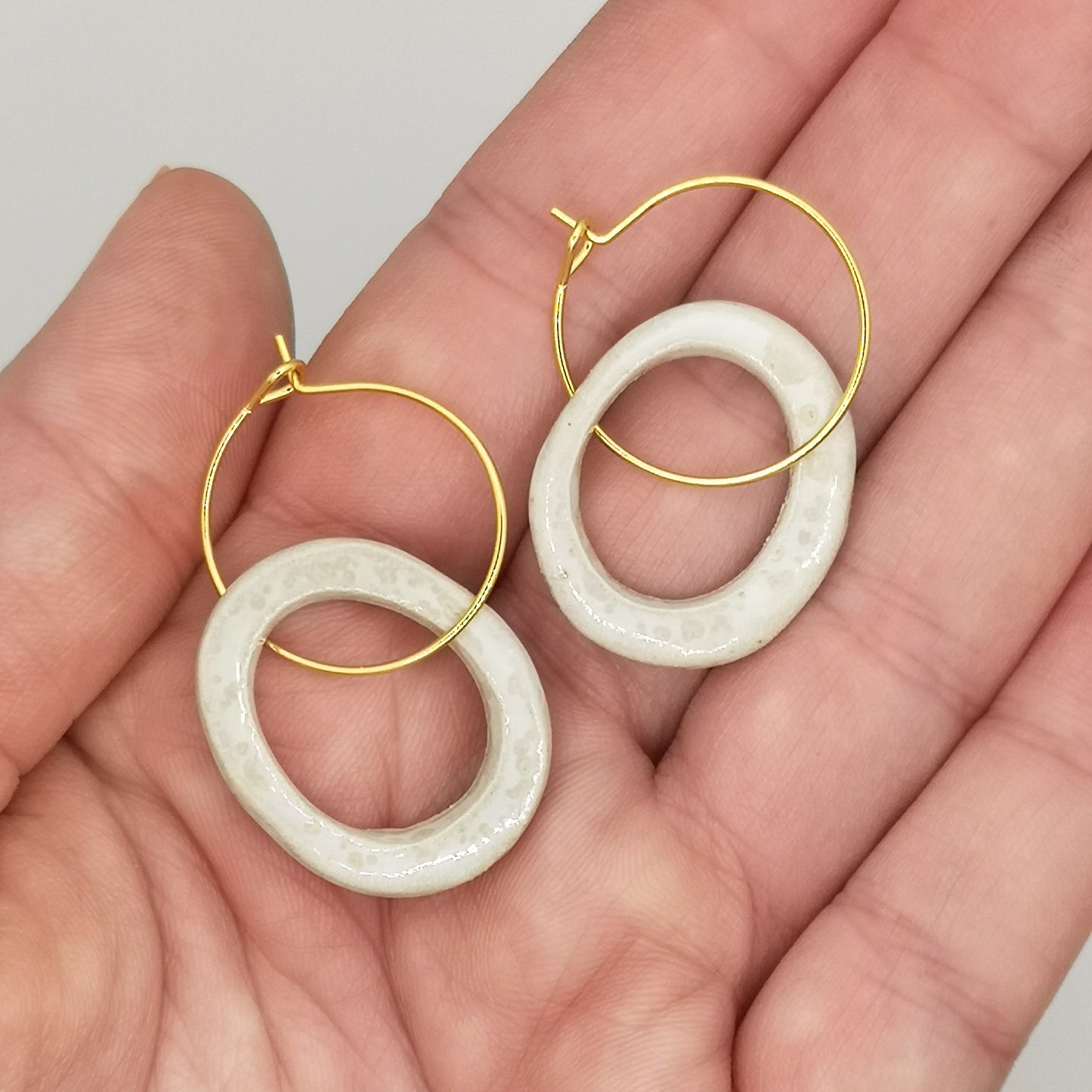 Gros plan des boucles d'oreilles en céramique blanche effet nacré avec anneaux dorés