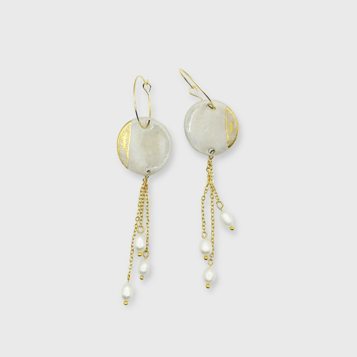 Boucles d'oreilles pendantes en céramique blanc nacré et or avec perles scintillantes au bout des chaînes.