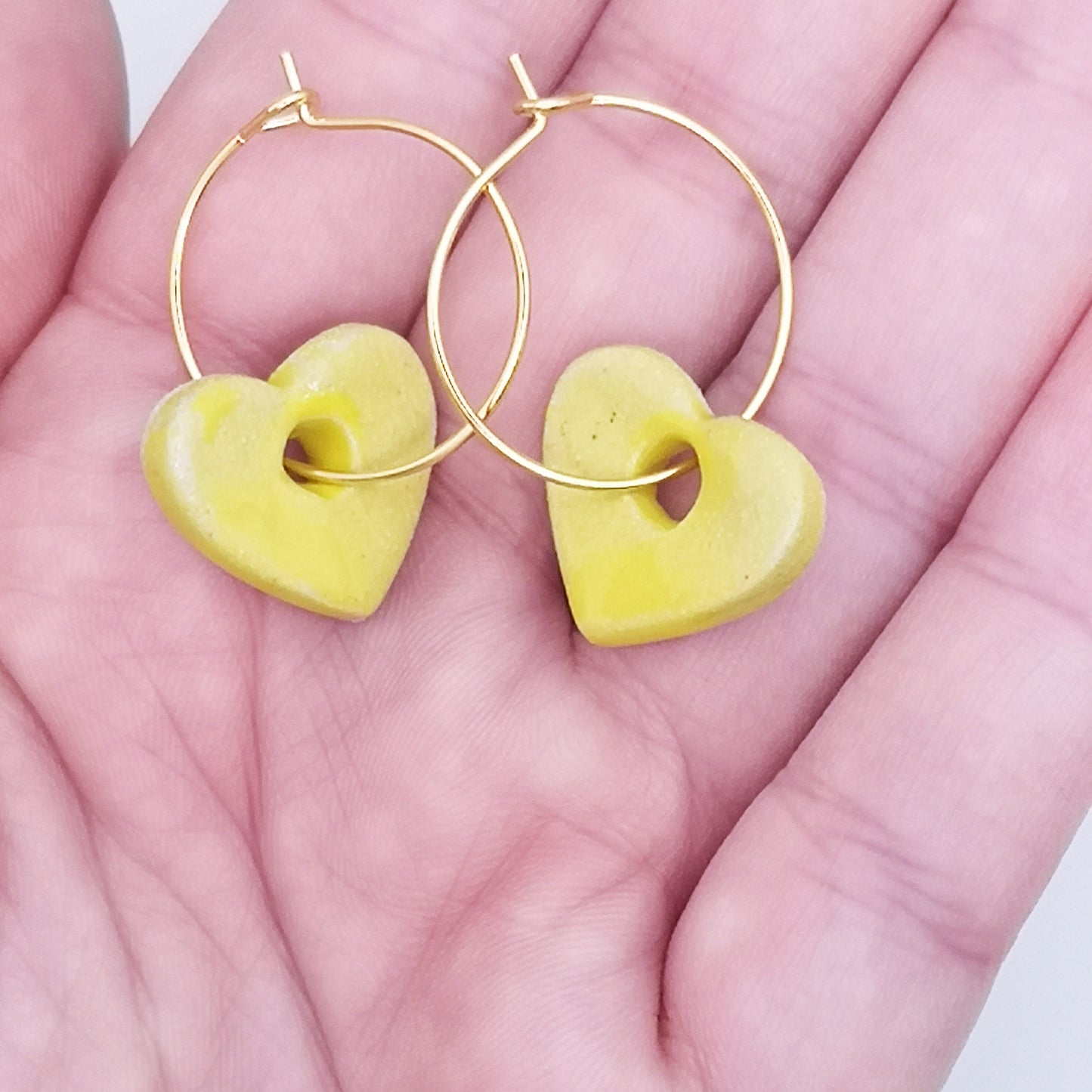 Vue rapprochée des boucles d'oreilles créoles avec pendentif cœur jaune vif en céramique, montées sur des anneaux en laiton doré à l'or fin. Bijoux artisanaux faits à la main en Provence.