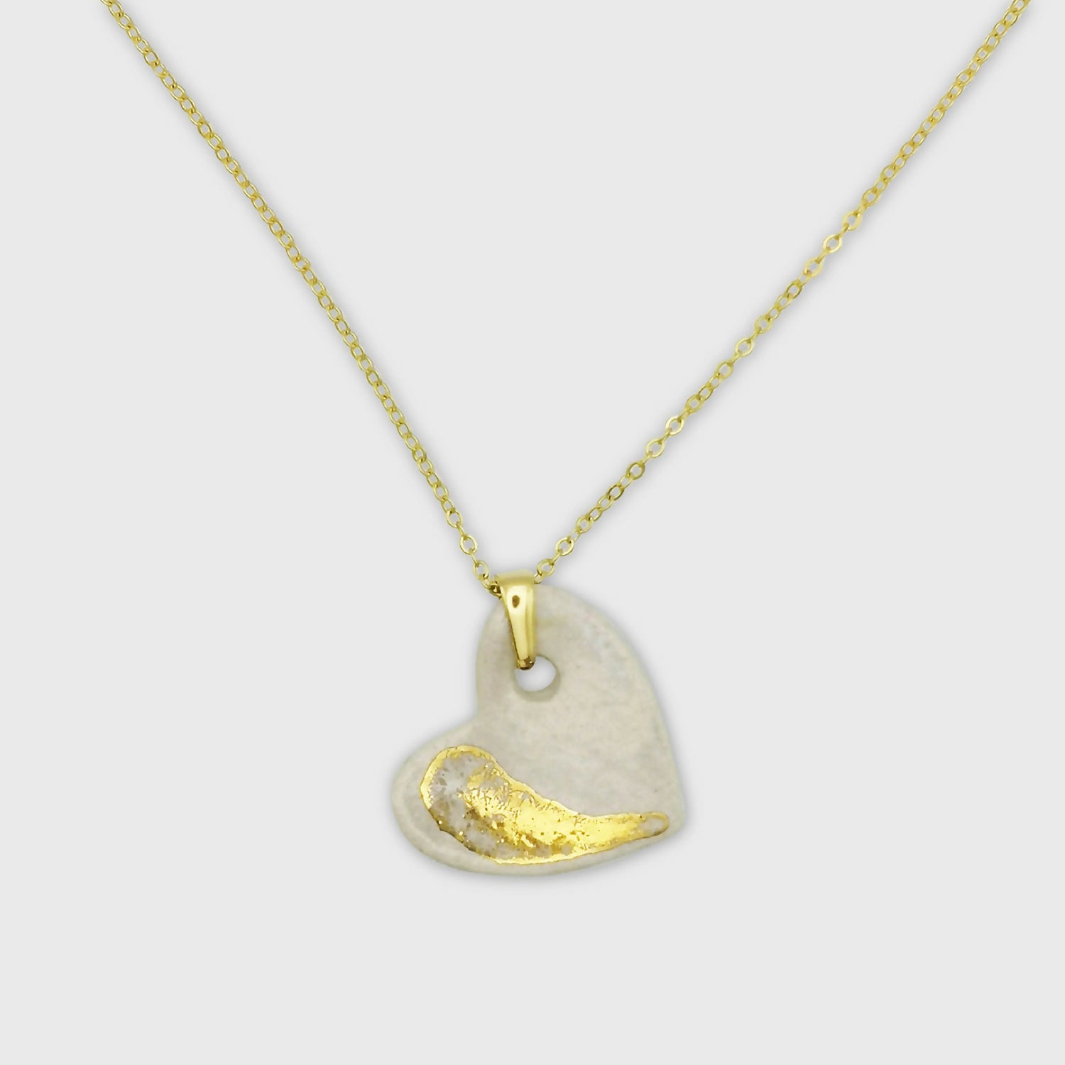 Collier cœur en céramique blanche nacrée et or avec chaîne en laiton doré, présenté sur fond neutre.
