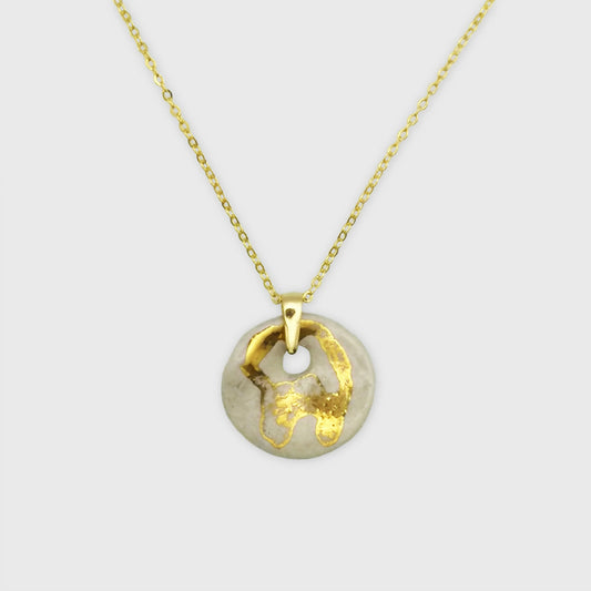 Collier médaillon blanc nacré et or avec pendentif en céramique fait main, présenté sur une surface élégante.