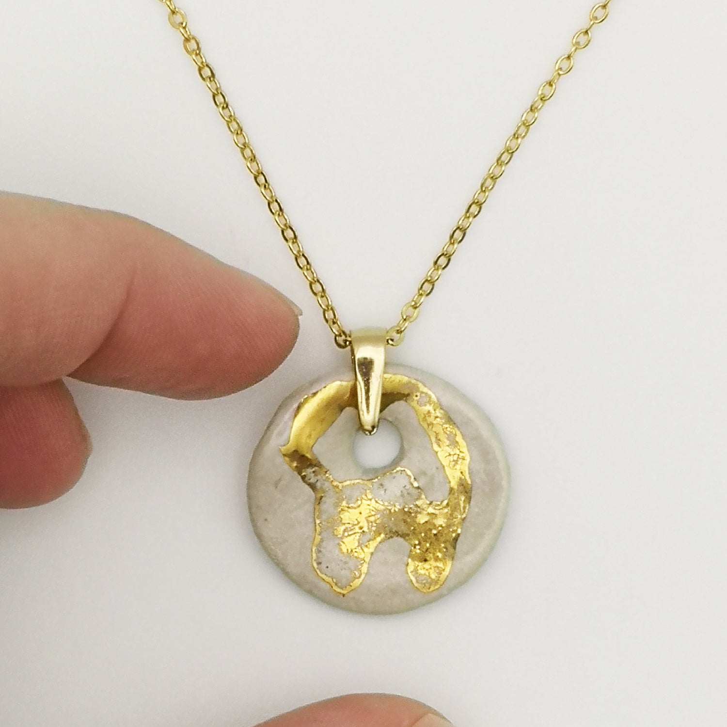 Zoom sur le pendentif médaillon blanc nacré avec dessins en or, collier artisanal unique idéal comme cadeau élégant.