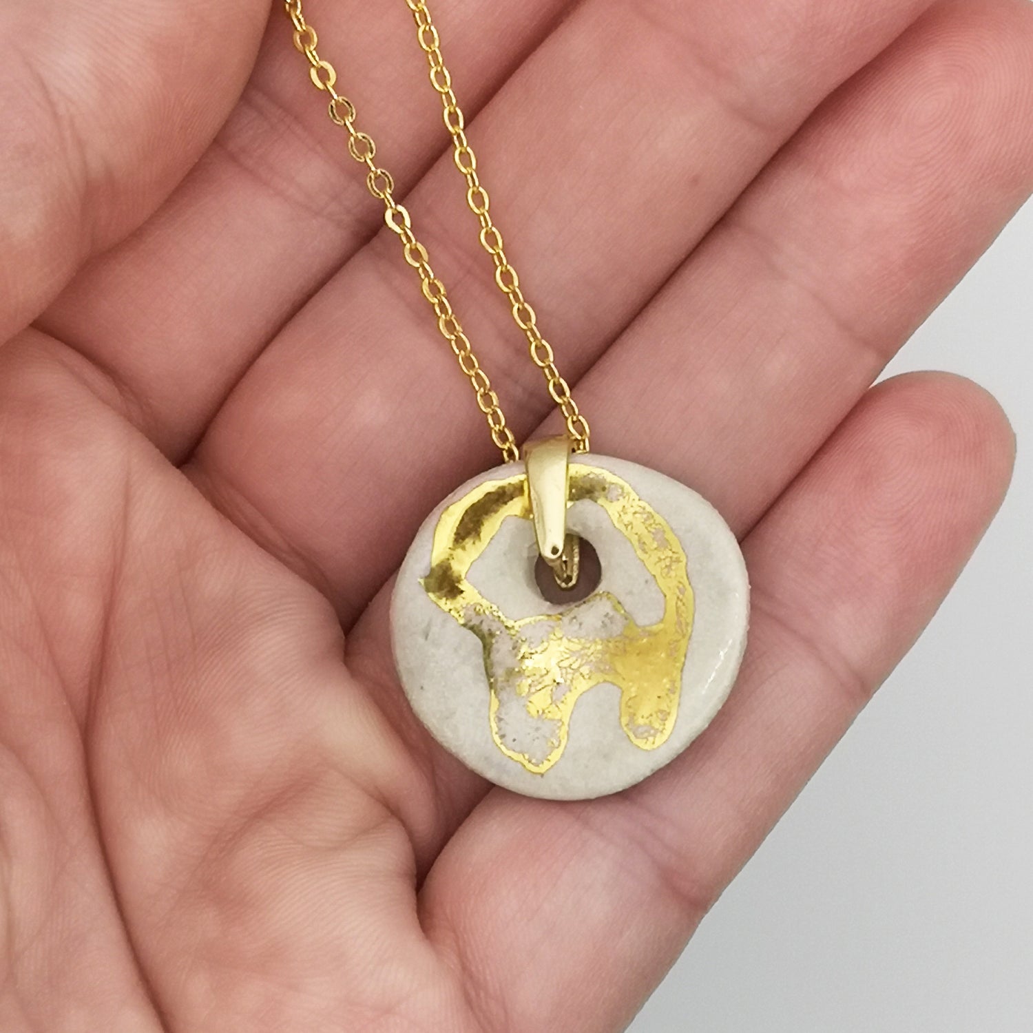 Détail du pendentif médaillon blanc effet nacré avec motif en or unique, suspendu à un cordon en cuir réglable.