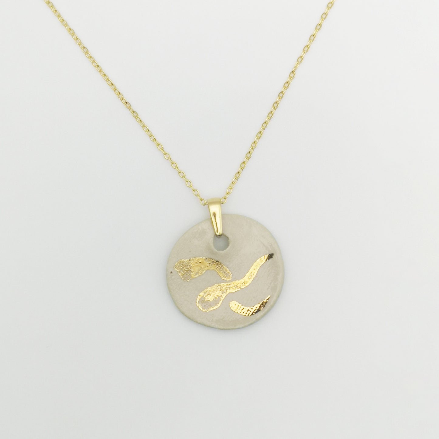 Collier médaillon blanc et or avec chaîne en laiton doré à l’or fin 24K – Pendentif rond en céramique blanche, orné d'un dessin "X" stylisé peint à la main avec de l'or véritable, sur une chaîne dorée élégante.