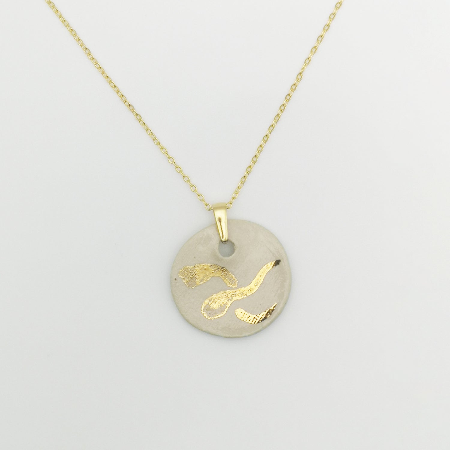 Collier médaillon blanc et or avec chaîne en laiton doré à l’or fin 24K – Pendentif rond en céramique blanche, orné d'un dessin "X" stylisé peint à la main avec de l'or véritable, sur une chaîne dorée élégante.