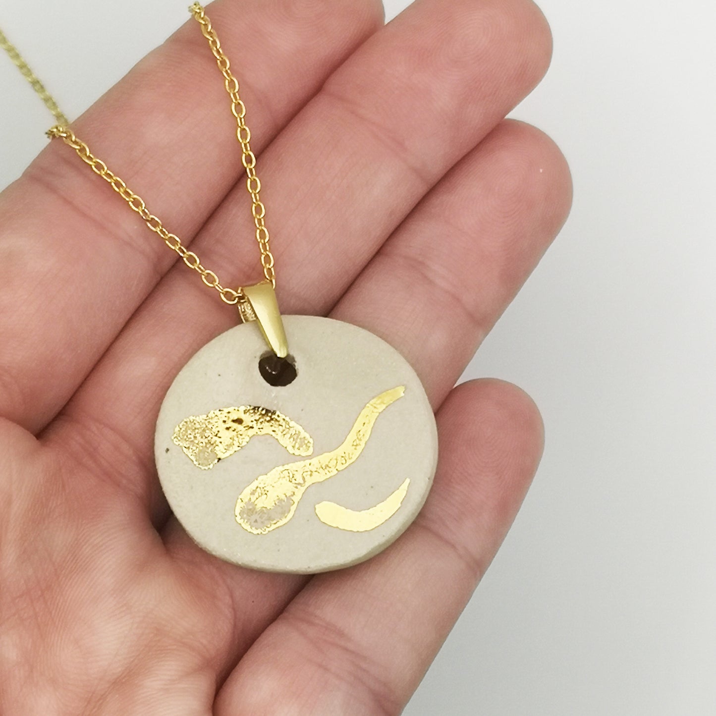 Détail du pendentif en céramique blanche du collier médaillon – Médaillon en argile cuite recouvert d’émail transparent, avec un motif en or véritable peint à la main, apportant un effet brillant et raffiné.