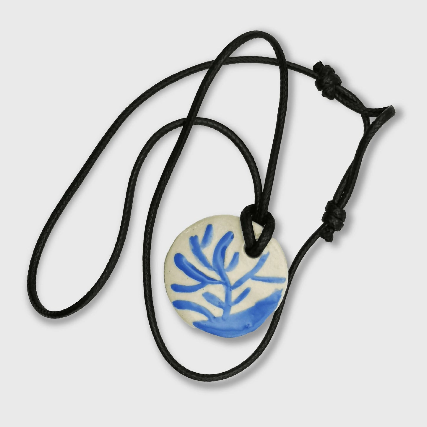 Collier médaillon en céramique blanc et bleu avec motif branche dorée, sur long cordon en cuir réglable, inspiration nature, bijou artisanal uni