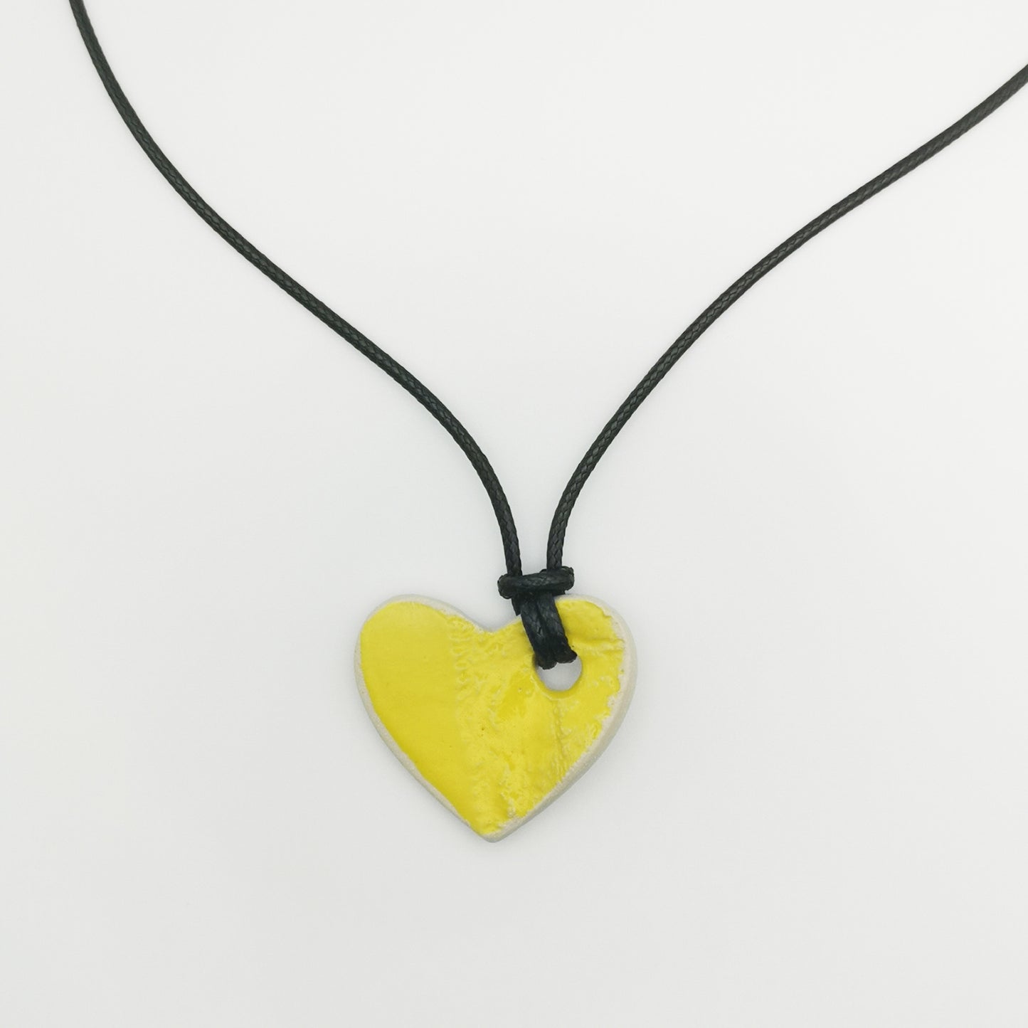 Collier cœur jaune en grès avec motifs gravés, suspendu sur un cordon en cuir, présenté dans un écrin rose pâle