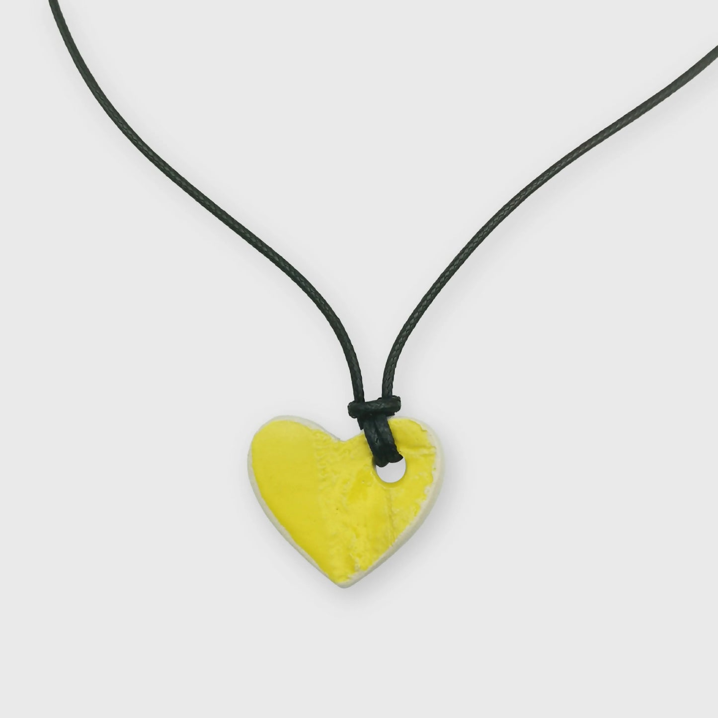 Collier cœur jaune en grès avec motifs gravés, suspendu sur un cordon en cuir, présenté dans un écrin rose pâle