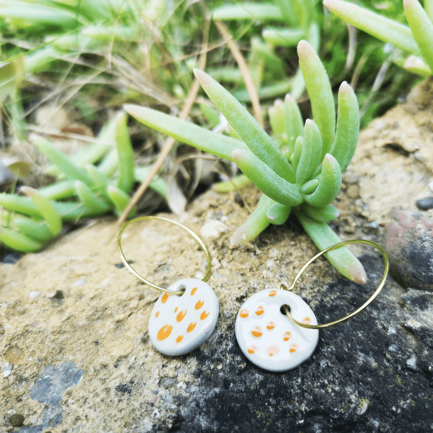 Boucles d'oreilles blanche a pois orange sur rocher avec plante verte
